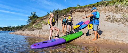 A guide showing a group of paddleboarders colorful paddleboards on a sandy riverside beach.
